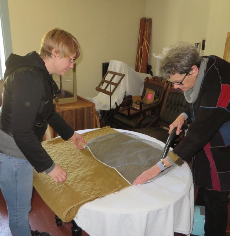 Katie Likens, left, a graduate student at the University of Rhode Island, and JoAnn Stabb, professor emerita, University of California at Davis, use a special vacuum to clean one of Lincoln County Historical Association’s 18th century quilts. The soft mesh screen prevents fibers from breaking. Courtesy of Christine Hopf-Lovette