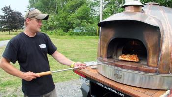 ERIC CORNELL takes a finished pizza out of the wood-fired copper oven used at CRUST. SUZI THAYER/Boothbay Register