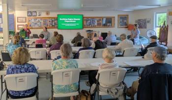 Boothbay Region Climate Action Team chair Louise Cowan, standing left, speaks to Boothbay and Boothbay Harbor residents before a Sept. 16 talk from Boothbay Region Emergency Management Director John Oakes. Photo by Sunrise Ecologic Boothbay Region Climate Action Team chair Louise Cowan, standing left, speaks to Boothbay and Boothbay Harbor residents before a Sept. 16 talk from Boothbay Region Emergency Management Director John Oakes. Photo by Sunrise Ecologic.