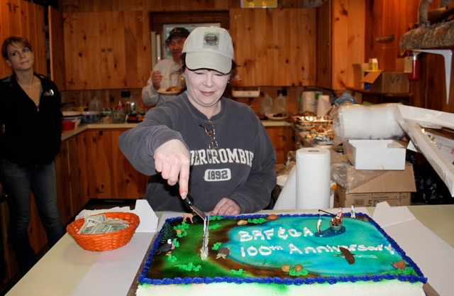 President Tammy Steinmetz cuts the Fish and Game Association’s 100th birthday cake at the clubhouse on Wiley Pond. The cake featured Wiley Pond, a fishermen with hooked fish, as well as an eagle, beaver, snapping turtle, duck and river otter. Below: Sophia Stark and Treasurer Keith Royal. SUE MELLO/Boothbay Register President Tammy Steinmetz cuts the Fish and Game Association’s 100th birthday cake at the clubhouse on Wiley Pond. The cake featured Wiley Pond, a fishermen with hooked fish, as well as an eagle, beaver, snapping turtle, duck and river otter. SUE MELLO/Boothbay Register
