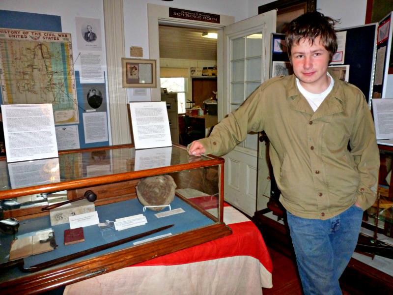 Devyn Campbell stands next to a glass case filled with Civil War artifacts he helped identify at the Boothbay Region Historical Society’s Civil War exhibit. KATRINA CLARK/Boothbay Register