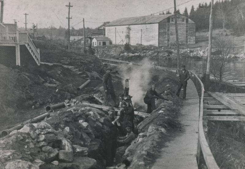 By late November 1912 Elbridge Giles's waterline pipe-laying crew had rounded Mill Cove and was headed for West Harbor. The photo's largest feature is the Mill Cove Ice Company's icehouse, with its elevator rising to the top. The site's gentle hill was blasted level and covered with condominiums in the late 1980s. The 1900s ice run to the deepwater wharf is apparent; it looks like a little sidewalk running outside the obvious sidewalk. The poles in the cove constitute the fish weir of Clarence or Charles Hodgdon, meant to trap herring and alewives. Courtesy of Barbara Rumsey