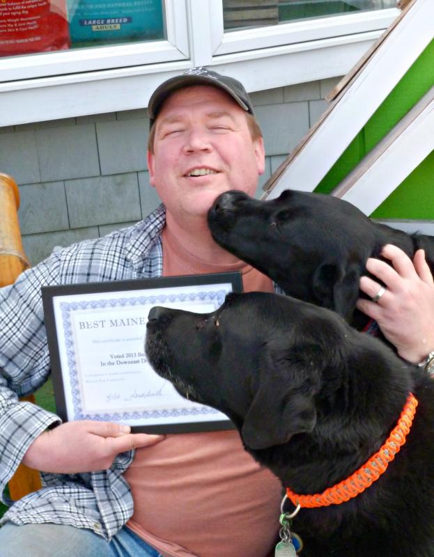Owner Don Kingsbury holds Two Salty Dog’s award from 2013, while labs Coal (front) and Max (rear) insist on getting attention. KATRINA CLARK/Boothbay Register
