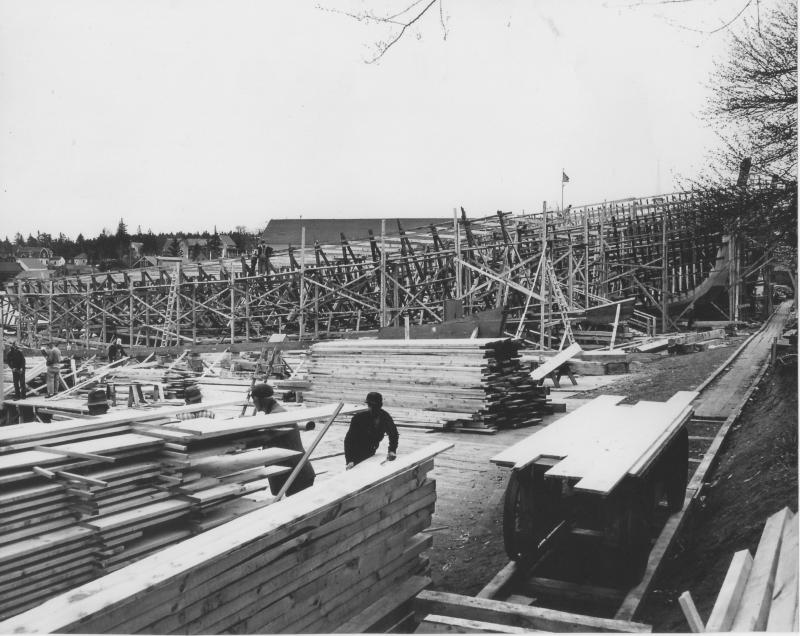 This 1953 East Boothbay view looks south to the Hodgdon yard building. The Lincoln Street yards are out of sight on the right. Four future minesweepers are shown, two with their tall stems in place on the far right, and two with their keels laid only. The men are working on extending the planking over the mudflats and on the scaffolding next to one of the skeletal ships. In the right foreground is the track and the handcar with short lengths of planking on top. Courtesy of Robert Rice