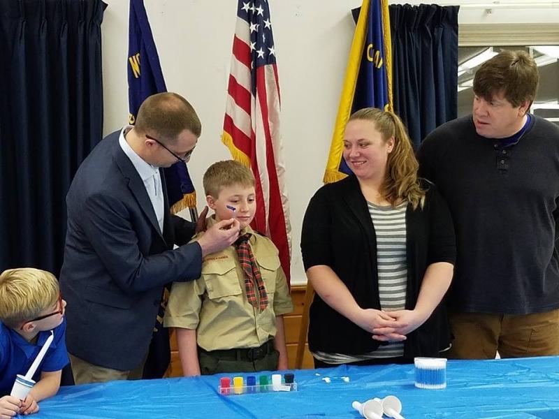 Grahm Cox’s dad Derrick paints a blue, gold and white stripe on his cheek during the boy’s Arrow of Light Ceremony on Feb. 24. Grahm’s mom Lauren is beaming while stepdad David Allen and younger brother Owen (far left) watch with great interest. Courtesy of Robin Ford