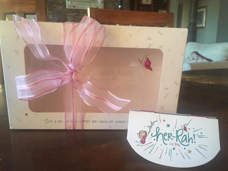 Packaging for the gift set in background; retail store identification in front. Her-Rah! First Bra