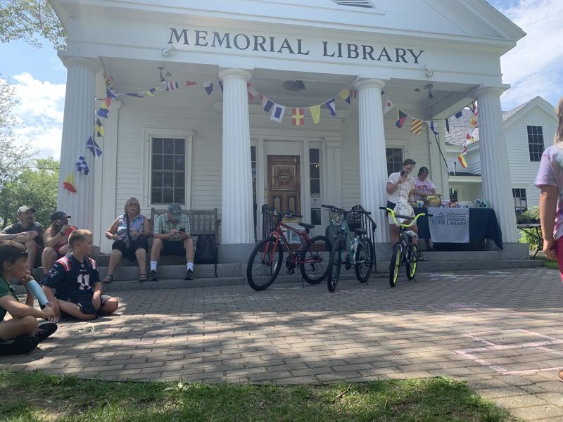 Bethany Schmidt holds the book bag prize while Jennifer Betts chooses the winning ticket from a golden cauldron. Three of the seven raffle prize bikes are showcased in the front. LILLY CURTIS/Boothbay Register