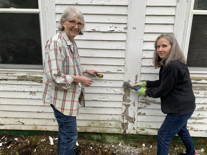 Saturday was too damp to paint, but Rebuilding Together volunteers Judy Adamson, left, and Rosemary Bourette scraped an Ocean Point Road home in preparation for painting later this month. BILL PEARSON/Boothbay Register