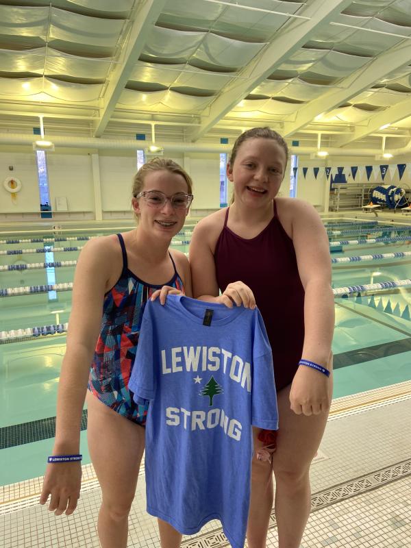 YMCA Dolphin swim team co-captains Hannah Hills, left, and Suzie Edwards hold up their support of Lewiston with their t-shirt and bracelets. Courtesy of BRYMCA