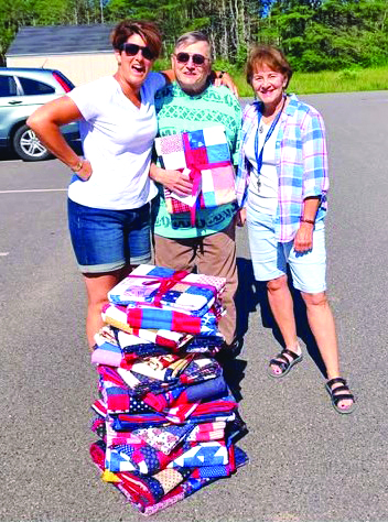 Erin Barter, left, veteran Ernie Gagnon and Cabin in the Woods Community Coordinator Auta Main stand by the 21 quilts ready to be distributed to veterans. Courtesy of VOA Northern New England Erin Barter, left, veteran Ernie Gagnon and Cabin in the Woods Community Coordinator Auta Main stand by the 21 quilts ready to be distributed to veterans. Courtesy VOA Northern New England