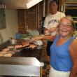 Lisa McSwain cooks the hamburgers and hot dogs while fellow Boosters Club member Andrew Morley brings more burgers to the grill during the August 31 home football game. KEVIN BURNHAM/Boothbay Register