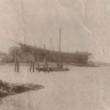 This April 1920 view shows the Machon house bobbing its way out of Mill Cove on its unmanned voyage to Tumbler Island. Small scows, such as that by the pilings, were fairly common. Perhaps it's the leaking one that set the house free, though it looks too small for half a house. The vessel being built on the shore of McFarlands Point at the Atlantic Coast Company is the 4-masted schooner James W. Howard, launched July 5, 1920. Courtesy of Lucille Machon