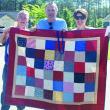 Bruce and Erin Barter help Tommy Schultz, Maine veteran and Cabin in the Woods resident (center) hold up one of the quilts that were made for veterans. Courtesy VOA Northern New England