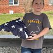 Andrew, son of Amanda and Andy Main, displays the properly folded American flag, purchased two years ago with funds raised by the 6th grade class of 2023. Courtesy photo