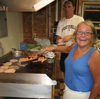 Lisa McSwain cooks the hamburgers and hot dogs while fellow Boosters Club member Andrew Morley brings more burgers to the grill during the August 31 home football game. KEVIN BURNHAM/Boothbay Register
