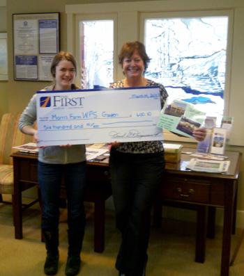 Abby Plummer, aka “Farm Abby” of the Morris Farm, left, accepts a check from Monique McRae, Wiscasset Branch Manager of The First for the Wiscasset Primary School’s garden project at the Morris Farm. Courtesy of The First