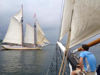 Ron Adolf, a passenger on the "Lewis R. French," hangs his feet over the bow as he watches the Heritage sail into Boothbay Harbor. RYAN LEIGHTON/Boothbay Register