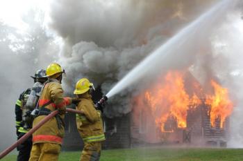 Firefighters tended Sunday’s house fire on Wiscasset Road, keeping it under control but not extinguishing it. Here firefighters douse a large evergreen tree to protect it from the blaze. SUE MELLO/Boothbay Register