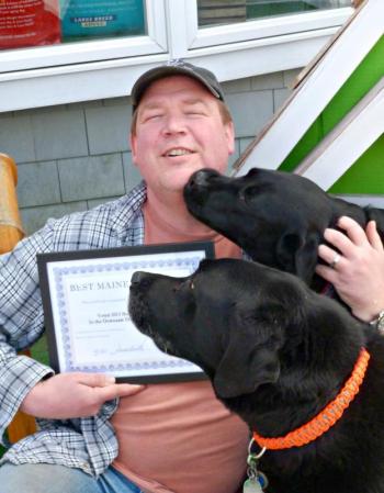 Owner Don Kingsbury holds Two Salty Dog’s award from 2013, while labs Coal (front) and Max (rear) insist on getting attention. KATRINA CLARK/Boothbay Register