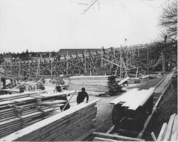 This 1953 East Boothbay view looks south to the Hodgdon yard building. The Lincoln Street yards are out of sight on the right. Four future minesweepers are shown, two with their tall stems in place on the far right, and two with their keels laid only. The men are working on extending the planking over the mudflats and on the scaffolding next to one of the skeletal ships. In the right foreground is the track and the handcar with short lengths of planking on top. Courtesy of Robert Rice