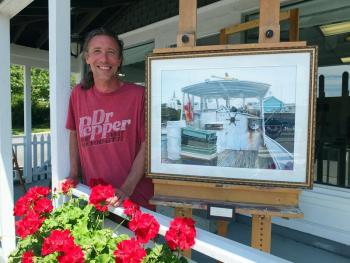 NATHAN CAMPBELL stands next to one of his favorite paintings, on the deck of his new Eastside Gallery at 26 Atlantic Avenue in Boothbay Harbor. SUZI THAYER/Boothbay Register