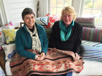 Kathleen Jones, left, and Diana Kerr of Kerr/Jones Design in Kerr’s sunroom in East Boothbay surrounded by their pillows, and holding a manta from Peru. SUZI THAYER/Boothbay Register