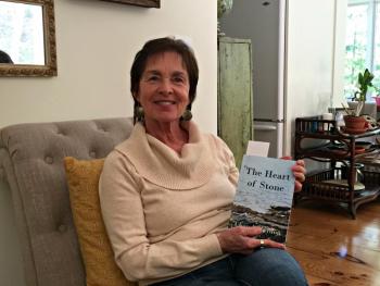Author Cheryl Blaydon in her East Boothbay home, holds a copy of her newest novel “The Heart of Stone.” KATRINA CLARK/Boothbay Register