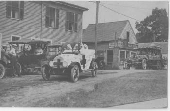This view of a circa 1920 patriotic parade, perhaps the 1919 "Welcome Come" parade, shows Oak Street by the current Capers building, across from the post office. The Capers building housed many businesses and apartments, including a funeral parlor. The Boothbay Register office was behind the site of the McDougall & Keefe photographic studio, now occupied by a car parts business. Both businesses moved frequently around town. I thank Robert Rice for identifying the autos: the Red Cross car is a 1917 Cadillac Model 55; the stationary car to the left is a 1915 Model T; while the rear car may be a 1918 Reo (named for Ransom E. Olds of Oldsmobile). Courtesy of the Boothbay Region Historical Society