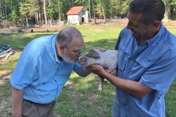 Boothbay Region Elementary School Principal Mark Tess kisses a two-day old piglet while the piglet’s owner, Seth Lewis, holds him. Courtesy of Lauren Brown/BRES