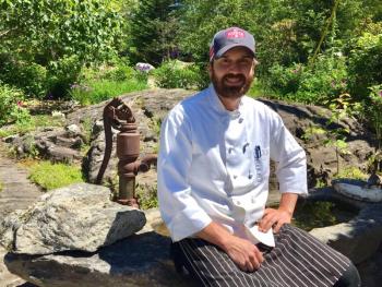 Chef Kelly Patrick Farrin outside his Carriage House Restaurant in East Boothbay. He’s sitting on a stone birdbath made by his father, Pat Farrin. SUZI THAYER/Boothbay Register