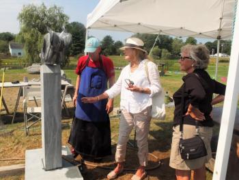 Two of the visitors to Boothbay Railway Village talk with stone sculptor Dick Alden about his piece. LISA KRISTOFF/Boothbay Register Dick Alden, East Boothbay ME