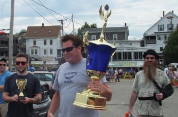Chris Gleason carries the Tug Across the Harbor trophy to the June 30 event. Darrell Gudroe, co-emcee, far right. LISA KRISTOFF/Boothbay Register