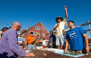Maine Champion Oyster Shucking Contest emcee Larry Sidelinger (standing center) calls the action as two contestants await the start of their heat at a past Pemaquid Oyster Festival, scheduled this year for Sunday, Sept. 30 at Schooner Landing in Damariscotta. Supervising the activity (left) is David Seybold, the “Grand Kahuna” of the Maine Champion Oyster Shucking Contest. Courtesy of scottbsmith.com