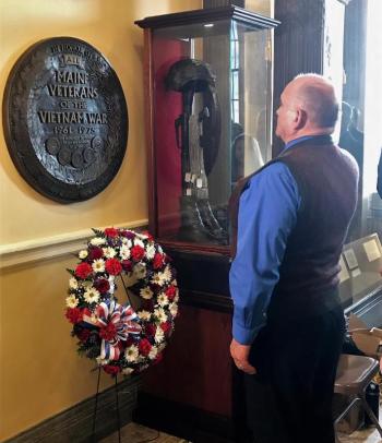 Ross Maddocks, a two-tour Vietnam Veteran, presents the ceremonial red, white and blue wreath and places it beneath the Maine Vietnam War Plaque in the Hall of Flags. Sarah Sherman photo