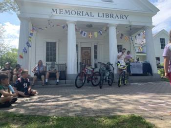 Bethany Schmidt holds the book bag prize while Jennifer Betts chooses the winning ticket from a golden cauldron. Three of the seven raffle prize bikes are showcased in the front. LILLY CURTIS/Boothbay Register