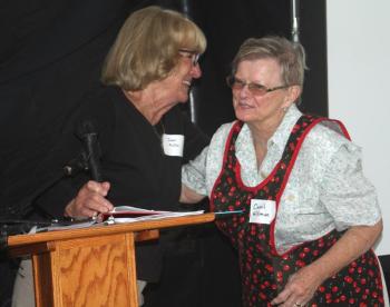 Jean McKay brings Carol Hillman up to the podium dressed as Mama/Ann Muise from the Living History Tour, a role McKay also portrayed. STEVE EDWARDS/Boothbay Register