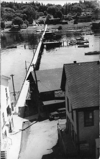 It’s difficult to get a good view of the footbridge. This one from the 1940s or 1950s looks to the east side of Boothbay Harbor. In the foreground is the north end of the Romar bowling alley. Halfway across the footbridge is the bridge house near the dock and float extending south. The house is obscured by being so dark. Courtesy of BRHS