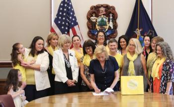 Finding Our Voices survivors and supporters flank Governor Janet T. Mills as she ceremoniously signs a bill initiated by the grassroots nonprofit into law. LD 692 brings safety to women and children survivors of domestic abuse. From left are Adeline and Eva with mom Nicole LeProhon, Jeannine Lauber Oren, Rep. Vicki Doudera, Governor Mills, Eliza Conley Lepene, Sandra Goulet, Dezarae Caron, Dana Ward, Meg Libby, Finding Our Voices founder and president Patrisha McLean, Kerrie McAnulty, Mary Kamradt, and Jennifer Greensmith. Jessi Tracy photo