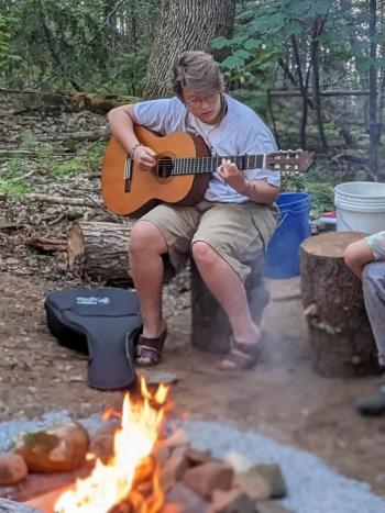 Olive Pine performs during a “First Fire” ceremony for Hearty Roots guests. CANDI JONETH/Boothbay Register Guitar playing