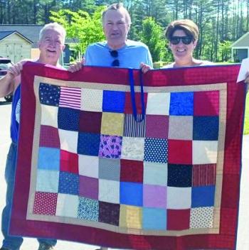 Bruce and Erin Barter help Tommy Schultz, Maine veteran and Cabin in the Woods resident (center), hold up one of the quilts made for veterans. Courtesy VOA Northern New England Bruce and Erin Barter help Tommy Schultz, Maine veteran and Cabin in the Woods resident (center) hold up one of the quilts that were made for veterans. Courtesy VOA Northern New England
