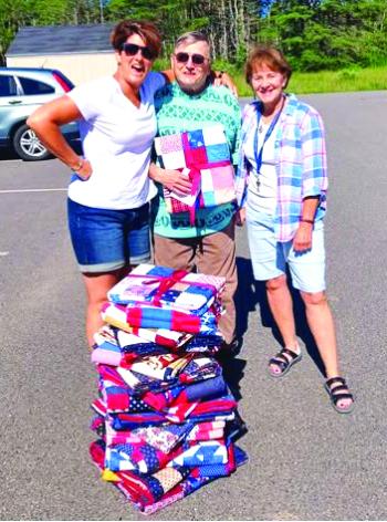 Erin Barter, left, veteran Ernie Gagnon and Cabin in the Woods Community Coordinator Auta Main stand by the 21 quilts ready to be distributed to veterans. Courtesy of VOA Northern New England Erin Barter, left, veteran Ernie Gagnon and Cabin in the Woods Community Coordinator Auta Main stand by the 21 quilts ready to be distributed to veterans. Courtesy VOA Northern New England