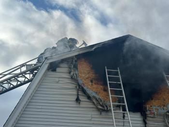 A firefighter chops a hole on the roof of the garage to gain access for water. Mark Sullivan photo Firefighter