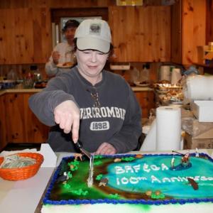 President Tammy Steinmetz cuts the Fish and Game Association’s 100th birthday cake at the clubhouse on Wiley Pond. The cake featured Wiley Pond, a fishermen with hooked fish, as well as an eagle, beaver, snapping turtle, duck and river otter. SUE MELLO/Boothbay Register