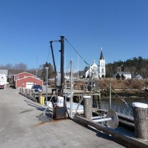 The Fish Pier of Boothbay Harbor. of Boothbay Harbor. The white and red buildings in the background on the left will be demolished and rebuilt when new construction begins. The crane in the foreground loads heavy barrels of bait onto waiting lobster boats. KATRINA CLARK/Boothbay Register