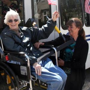 Jean McVicker, of Boothbay Harbor, waves an American flag as she is lifted into a new St. Andrews Village bus May 13 with the assistance of Village Activities Director Jerie Phinney. Courtesy of Lincoln County Healthcare