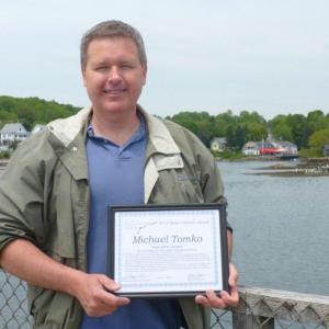 Local activist Mike Tomko stands on the footbridge in Boothbay Harbor with his award. “I’m very pleased that the selectmen and town manager of Boothbay Harbor have been talking about the footbridge improvement project,” Tomko said. “It’s such an iconic part of our town and can be a much bigger draw than it currently is.” KATRINA CLARK/Boothbay Register Local activist Mike Tomko stands on the footbridge in Boothbay Harbor with his award. “I’m very pleased that the selectmen and town manager of Boothbay Harbor have been talking about the footbridge improvement project,” Tomko said. “It’s such an iconic part of our town and can be a much bigger draw than it currently is.” KATRINA CLARK/Boothbay Register