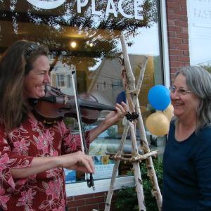 Liz Lannon, left, of Wiscasset on fiddle meets up with twig artist Susan Perrine of Woolwich outside Mac's Place during the art walk. SUSAN JOHNS/Wiscasset Newspaper