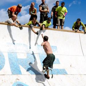 Wounded warrior Noah Galloway soars up “Everest” as Jason Nein (left) and Jared Mitkus (with mohawk) reach down to help him over. Karen Colby stands directly behind Mitkus. Courtesy of Tough Mudder photographer, Dmitry Gudkov. Wounded warrior Noah Galloway soars up “Everest” as Jason Nein (left) and Jared Mitkus (with mohawk) reach down to help him over. Karen Colby stands directly behind Mitkus. Courtesy of Tough Mudder photographer, Dmitry Gudkov.