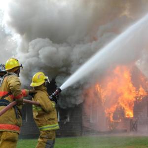 Firefighters tended Sunday’s house fire on Wiscasset Road, keeping it under control but not extinguishing it. Here firefighters douse a large evergreen tree to protect it from the blaze. SUE MELLO/Boothbay Register