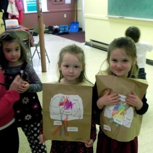Charlotte Abello practices using a stethoscope with her mother, while Audrey Strong and Eve Allen wear their circulatory system vests that they made in Seedling Explorers class. Courtesy of Seeds of Knowledge